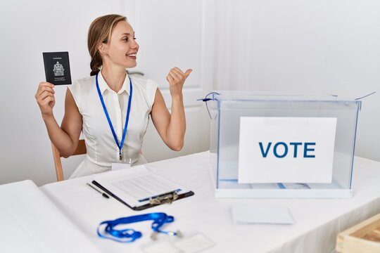 Young blonde woman at political campaign election holding canada passport pointing thumb up to the side smiling happy with open mouth