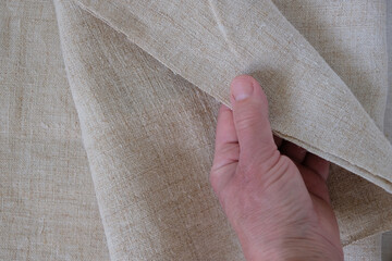 Human hand demonstrates natural hemp fabric. Growing demand for hemp products. Selective focus.
