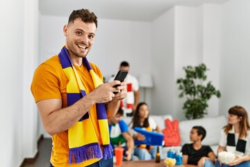 Group of young friends watching and supporting soccer match. Man smiling happy using smartphone at home.