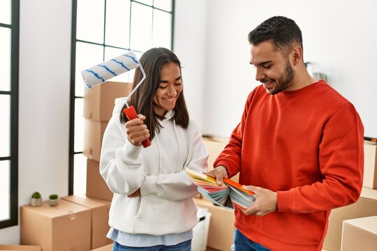 Young Latin Couple Painting Using Paint Roller At New Home.