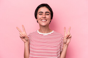 Young caucasian woman isolated on pink background showing victory sign and smiling broadly.