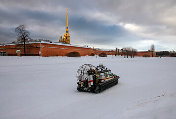 An aero-boat moves on the ice of the Kronverk Strait of the Neva against the background of the Peter and Paul Fortress and the Cathedral.