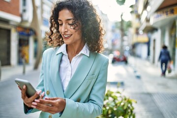 Young hispanic business woman wearing professional look smiling confident at the city using smartphone