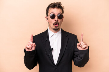 Young bodyguard caucasian man isolated on beige background pointing upside with opened mouth.