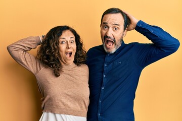 Fototapeta premium Middle age hispanic couple wearing casual clothes crazy and scared with hands on head, afraid and surprised of shock with open mouth
