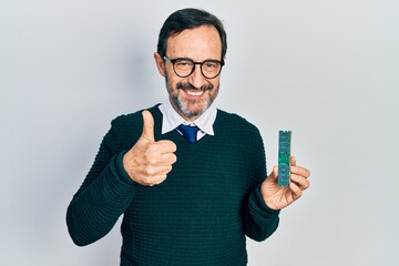 Middle age hispanic man holding memory ram smiling happy and positive, thumb up doing excellent and approval sign