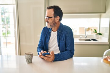 Middle age man using smartphone drinking coffee at home