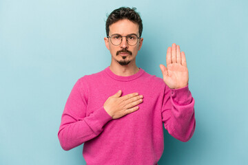 Young caucasian man isolated on blue background taking an oath, putting hand on chest.