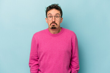 Fototapeta premium Young caucasian man isolated on blue background shrugs shoulders and open eyes confused.