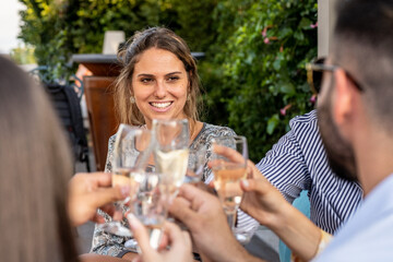 Attractive beautiful woman toasting and clinking with friends at celebration party, millennials lifestyle, outdoors summer event with elegant people drinking glasses of champagne