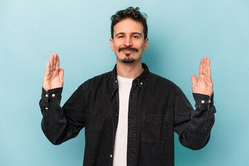 Young caucasian man isolated on blue background holding something little with forefingers, smiling and confident.