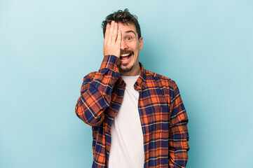 Young caucasian man isolated on blue background having fun covering half of face with palm.