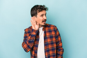 Young caucasian man isolated on blue background trying to listening a gossip.
