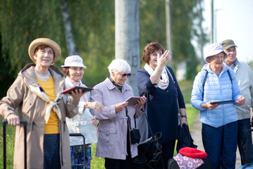 A group of happy senior friends with suitcases using tablet and waiting for a train on the platform