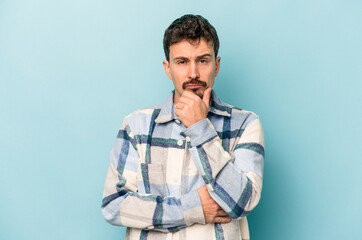 Young caucasian man isolated on blue background thinking and looking up, being reflective, contemplating, having a fantasy.