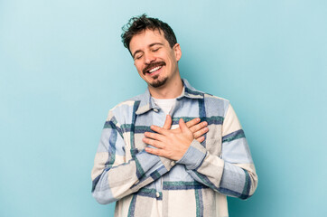 Obraz premium Young caucasian man isolated on blue background laughing keeping hands on heart, concept of happiness.