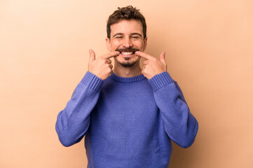 Young caucasian man isolated on beige background smiles, pointing fingers at mouth.