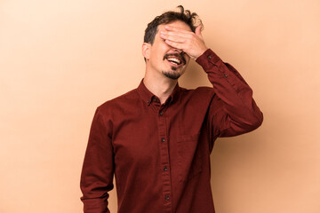 Young caucasian man isolated on beige background covers eyes with hands, smiles broadly waiting for a surprise.