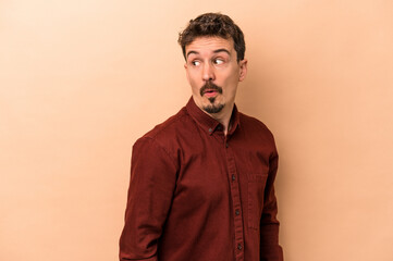 Fototapeta premium Young caucasian man isolated on beige background looks aside smiling, cheerful and pleasant.