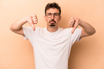 Young caucasian man isolated on beige background showing a dislike gesture, thumbs down....
