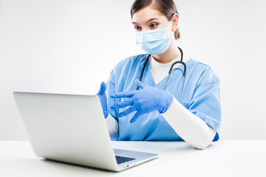 Young UK NHS Female Doctor Wearing Face Mask And Gloves Talking To Patient Over Laptop Computer