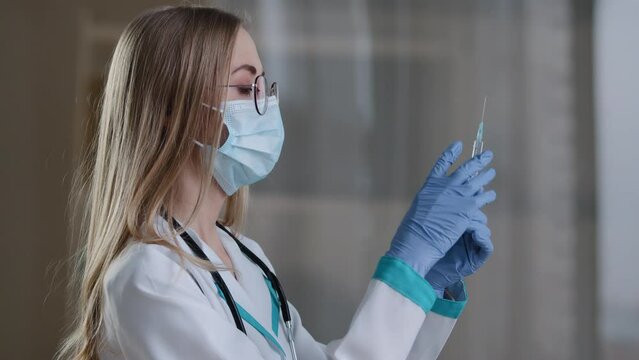 Woman doctor wearing a face mask and medical gown preparing holding syringe for injection covid19 vaccination. Female nurse with liquid medicine antibiotic flu antivirus vaccine protection from virus