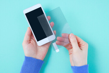 Protective film for the smartphone screen in the hands of a caucasian woman. Trying on smartphone. Berquoise background.