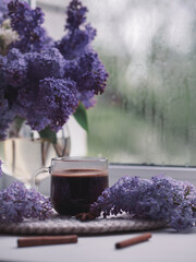 Obraz na płótnie Canvas A cup of coffee and a bouquet of lilacs on the windowsill. Rainy spring day