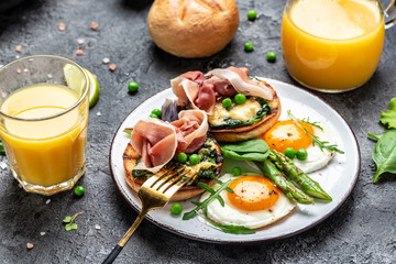 Traditional full English breakfast with grilled bun with spinach and cheese, asparagus, jamon, ham, prosciutto and fried egg. fresh juice. Balanced diet. top view