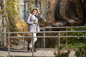 Portrait of attractive smiling middle-aged woman in checkered jacket and grey roll-neck sweater titivate hair on bridge.