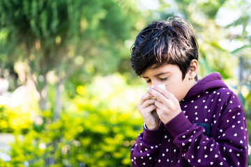 Young sick kid sneezing at park during winter - concept of seasonal winter illness, flu and...