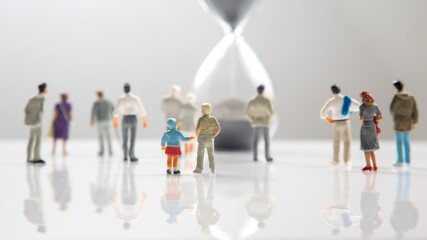 miniature people. different people are walking next to the hourglass on a white background....