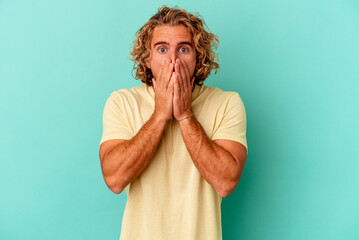 Young caucasian man isolated on blue background shocked, covering mouth with hands, anxious to discover something new. - obrazy, fototapety, plakaty