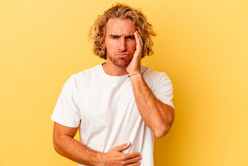 Young caucasian man isolated on yellow background blows cheeks, has tired expression. Facial expression concept.