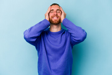Young caucasian man isolated on blue background laughs joyfully keeping hands on head. Happiness concept.
