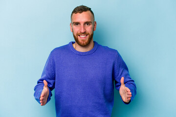 Young caucasian man isolated on blue background holding something with both hands, product presentation.