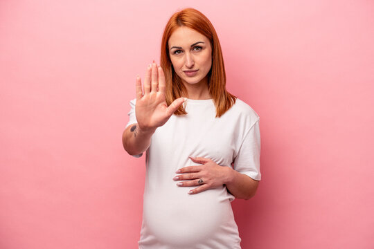 Young caucasian pregnant woman isolated on pink background standing with outstretched hand showing stop sign, preventing you.