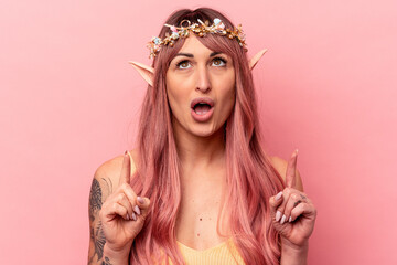 Young caucasian elf woman isolated on pink background pointing upside with opened mouth.