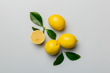 Many fresh ripe lemons with green leaves on colored background, top view, space for text