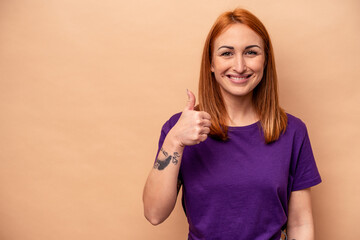 Young caucasian woman isolated on beige background smiling and raising thumb up