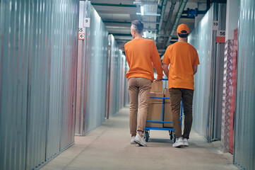 Workers wheeling the warehouse trolley with cardboard boxes