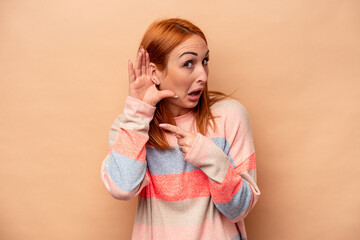 Young caucasian woman isolated on beige background trying to listening a gossip.