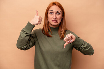 Young caucasian woman isolated on beige background showing thumbs up and thumbs down, difficult choose concept