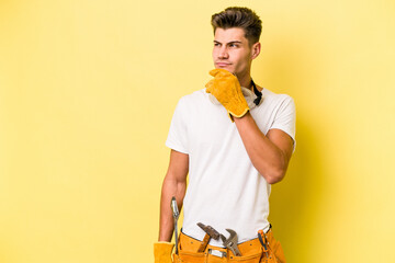 Young electrician caucasian man isolated on yellow background looking sideways with doubtful and...
