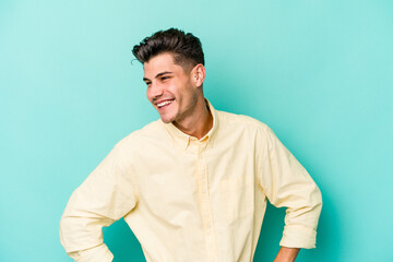 Young caucasian man isolated on blue background laughs happily and has fun keeping hands on stomach.