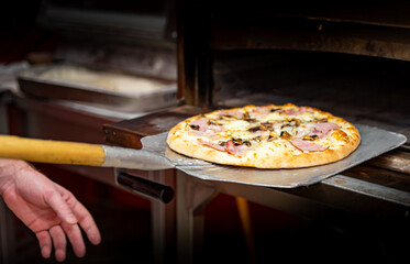 chef baker making pizza at kitchen. Put on landing shovel and send it to the oven.