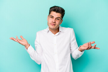 Young caucasian man isolated on blue background doubting and shrugging shoulders in questioning...