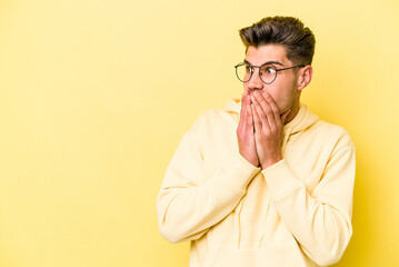 Young caucasian man isolated on yellow background thoughtful looking to a copy space covering mouth with hand.