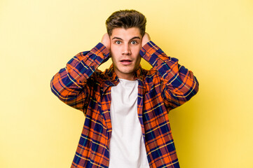 Young caucasian man isolated on yellow background covering ears with hands trying not to hear too loud sound.