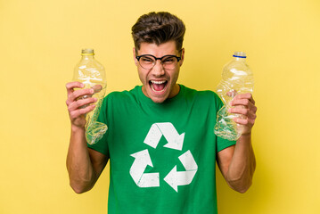 Young caucasian man holding a bottle of plastic to recycle isolated on yellow background